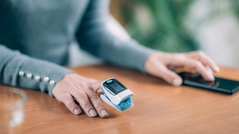 Lady's hand holding smartphone in one hand and using a blood oximeter on the other hand for Oximetry at Home