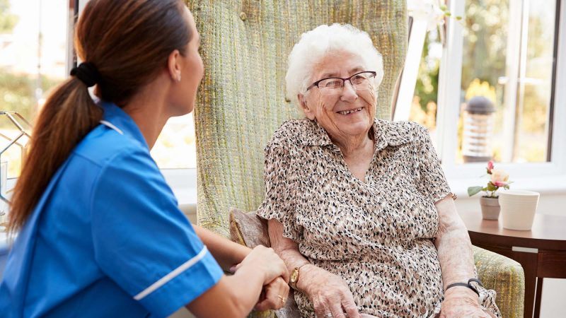 Nurse talking to smiling old lady sat in conservatory