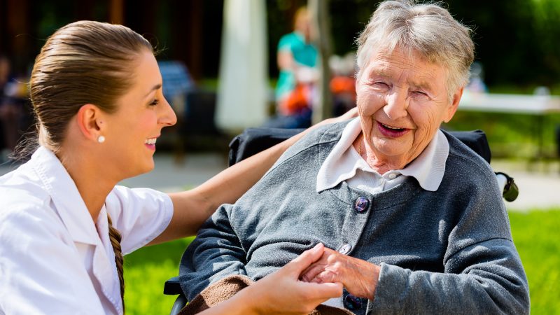 Nurse laughing and smiling with lady in her chair outside on a sunny day