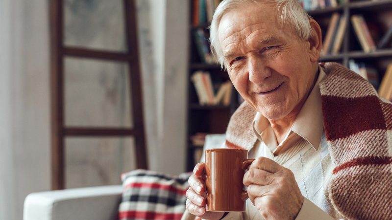 Elderly man enjoying a hot drink in his living room - helping p